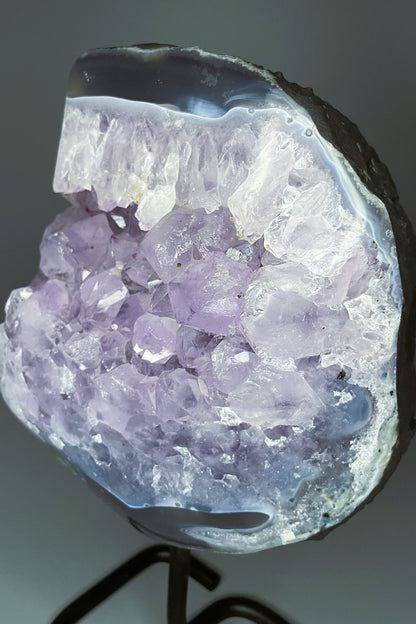 A Brazilian amethyst cluster with purple hues and large crystals on a black metal stand.