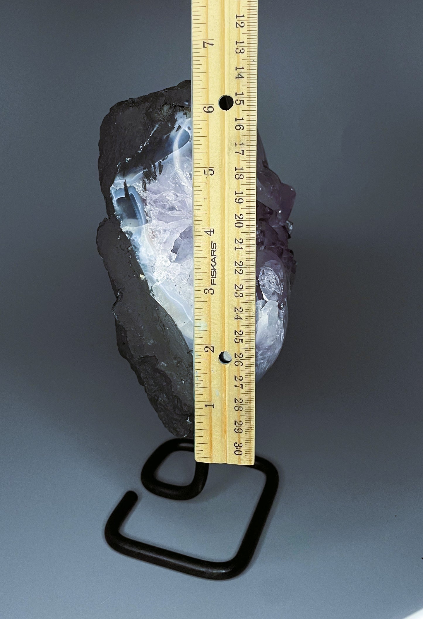 A Brazilian amethyst cluster with purple hues and large crystals on a black metal stand.