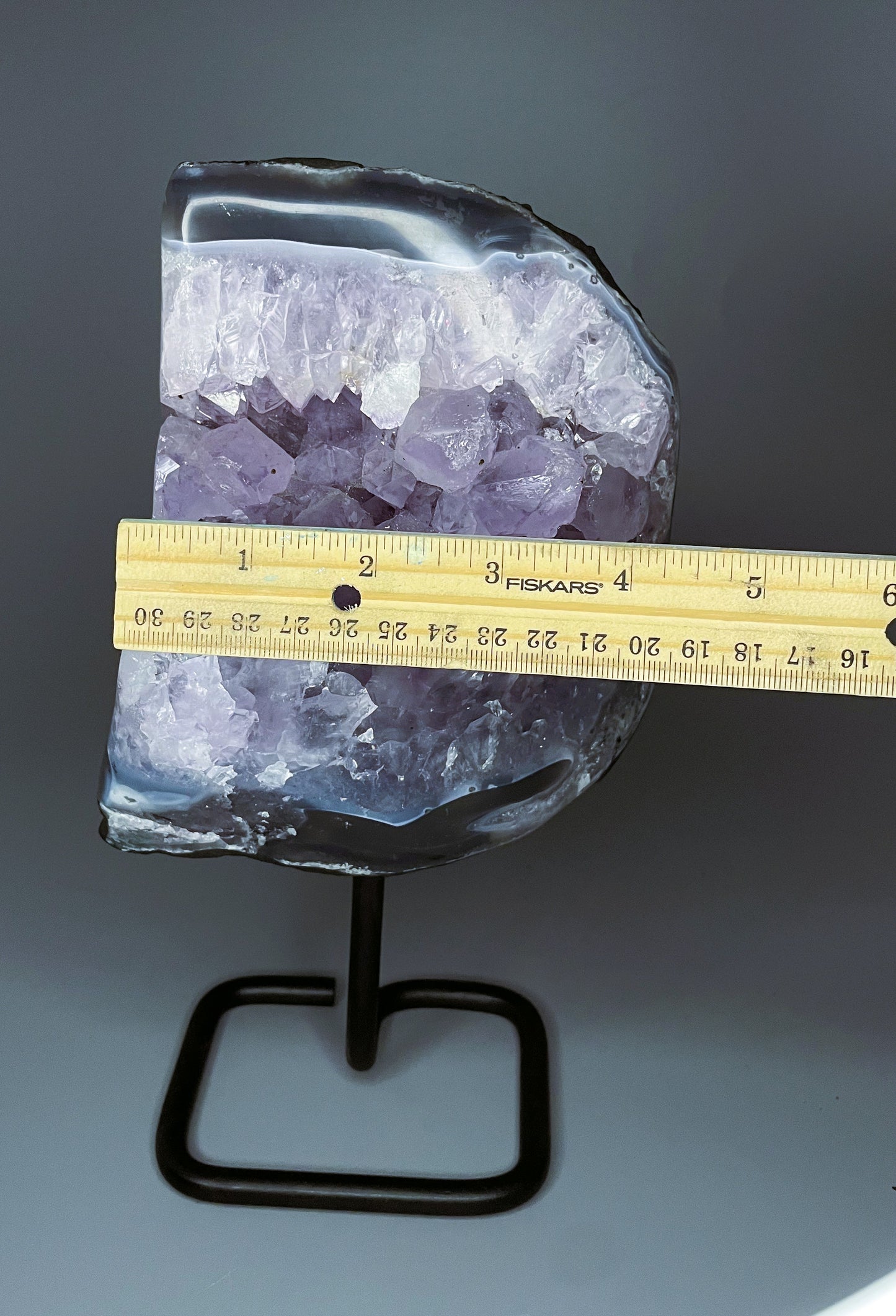 A Brazilian amethyst cluster with purple hues and large crystals on a black metal stand.