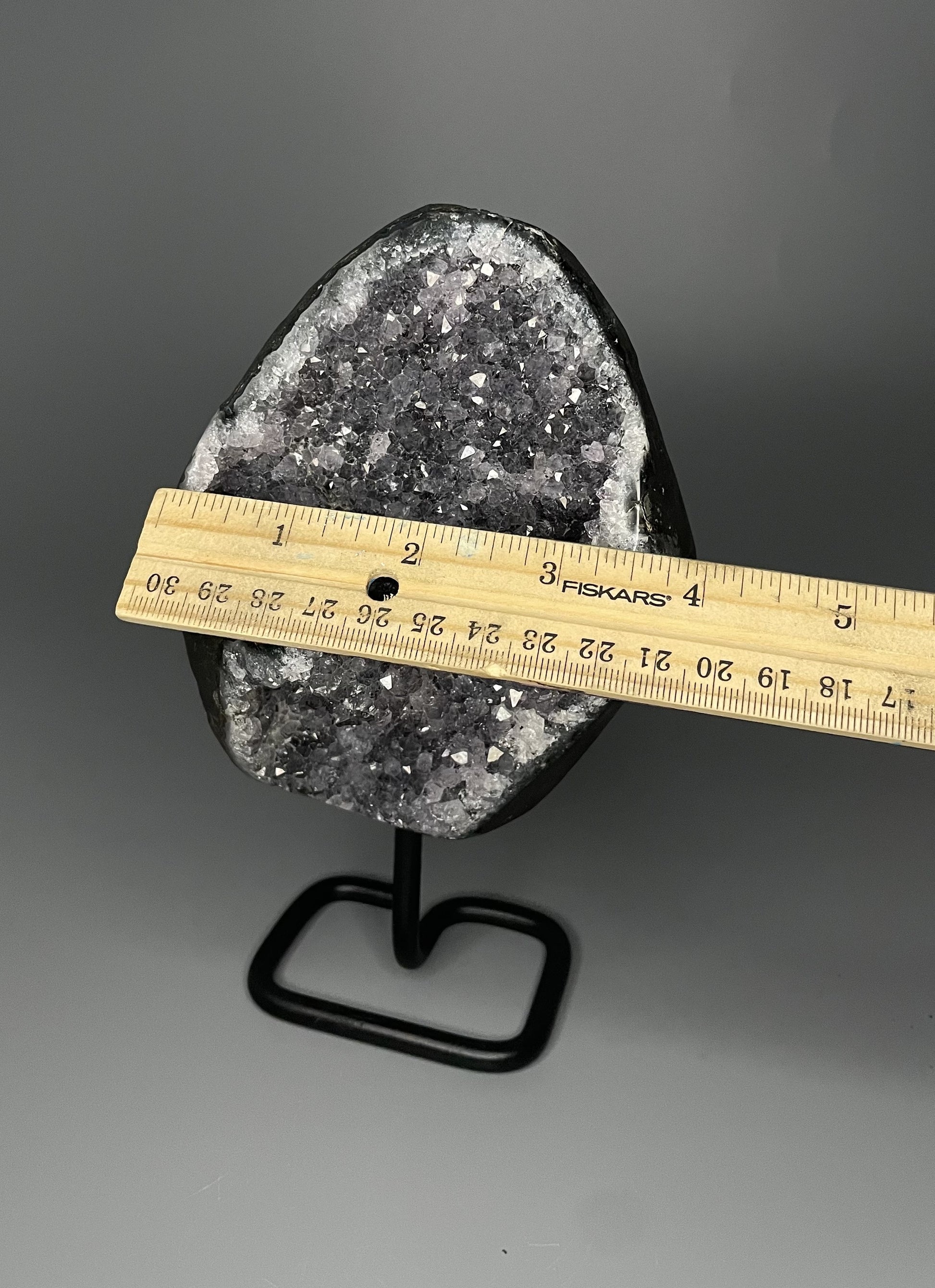 A Brazilian amethyst cluster with micro crystallization crystals on a black metal stand.