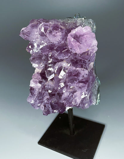 A Brazilian amethyst cluster with large crystals on a black metal stand.