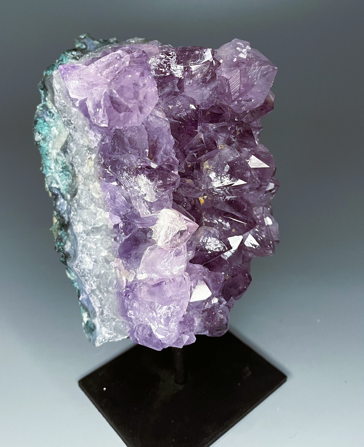 A Brazilian amethyst cluster with large crystals on a black metal stand.