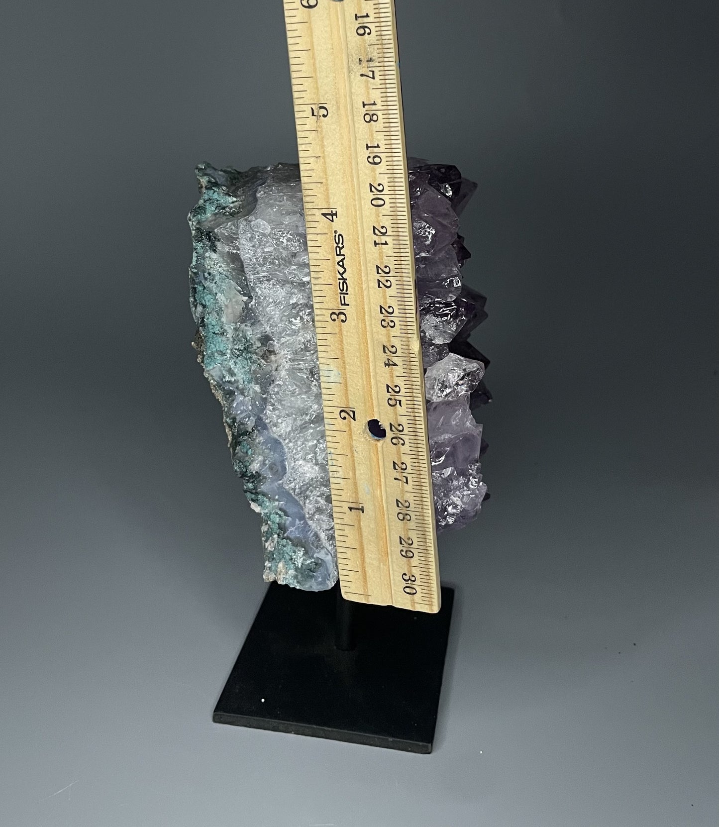 A Brazilian amethyst cluster with large crystals on a black metal stand.