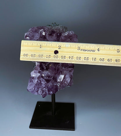 A Brazilian amethyst cluster with large crystals on a black metal stand.