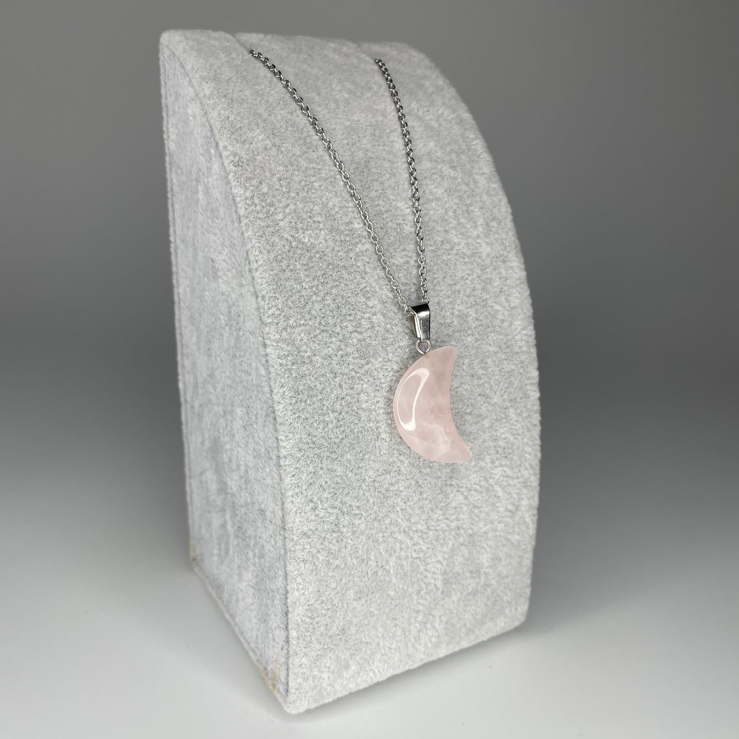 A 3 cm crescent moon pendant carved from various minerals hanging from a stainless steel chain