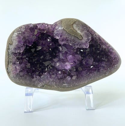 Amethyst cluster with polished edges and brilliant hues of deep purple and various sizes of crystal formations on a white background.