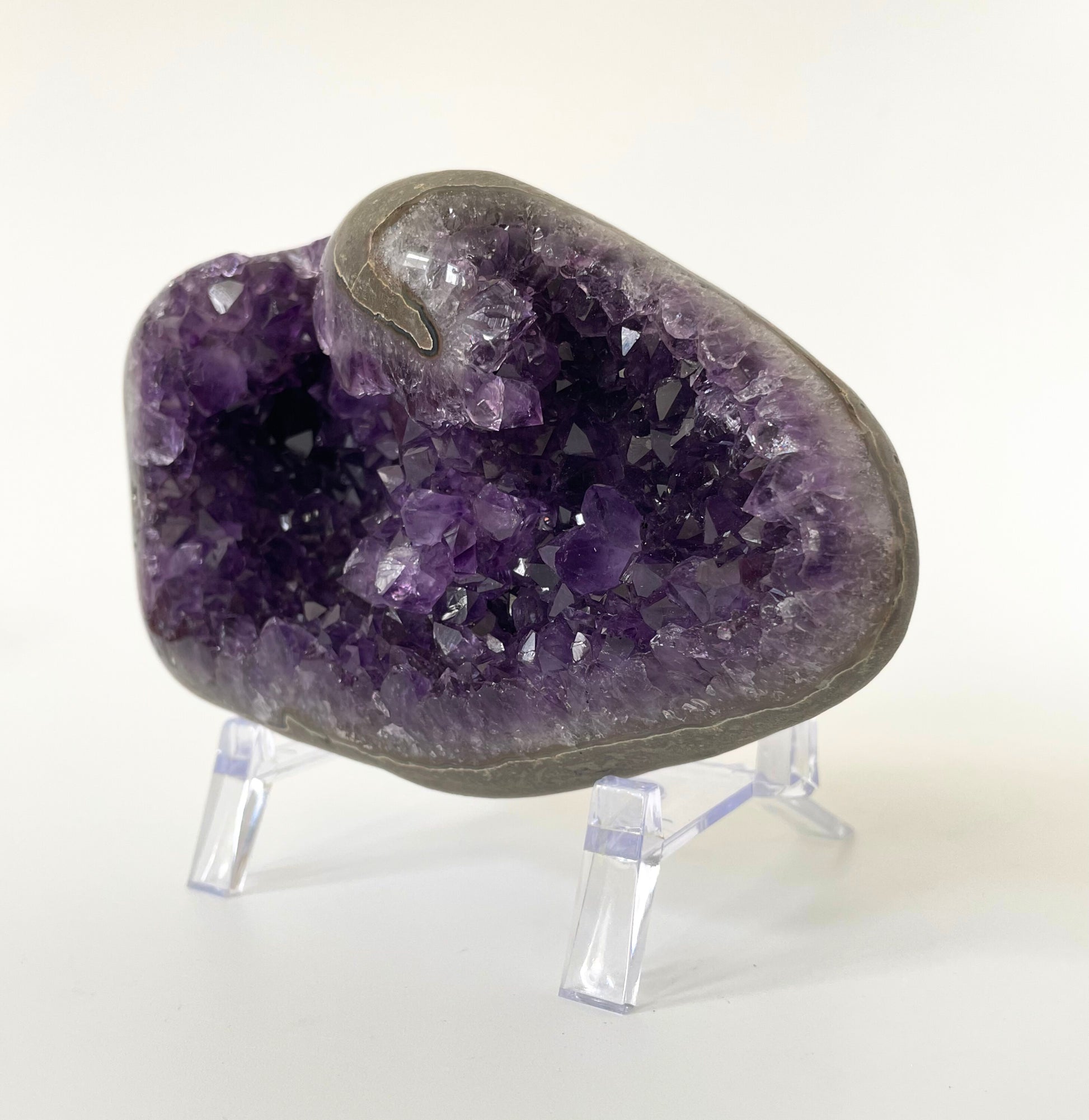 Amethyst cluster with polished edges and brilliant hues of deep purple and various sizes of crystal formations on a white background.