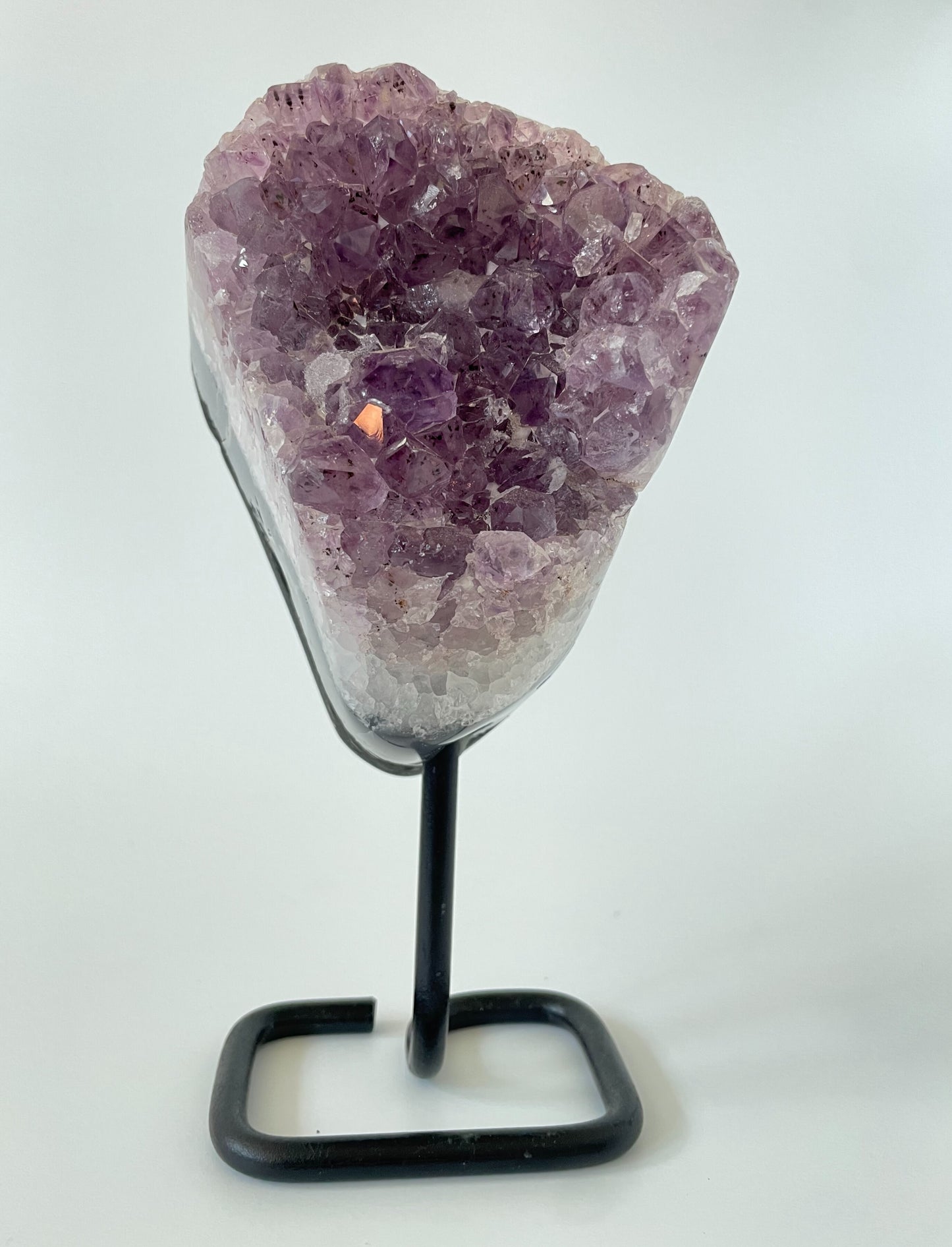 A 4-inch Brazilian amethyst cluster with purple hues and large crystals on a black metal stand with a white background.