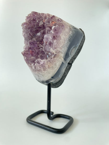 A 4-inch Brazilian amethyst cluster with purple hues and large crystals on a black metal stand with a white background.