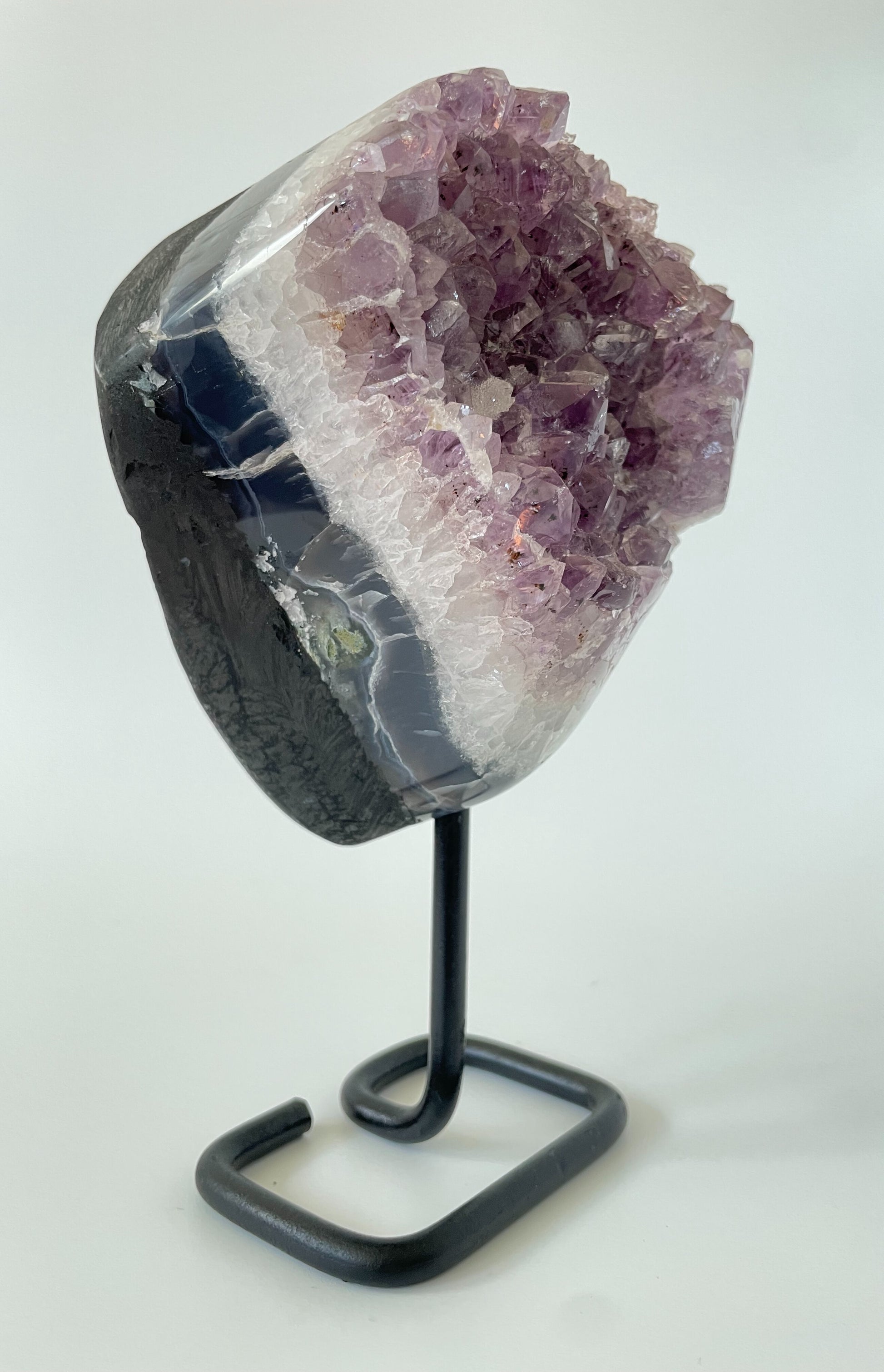 A 4-inch Brazilian amethyst cluster with purple hues and large crystals on a black metal stand with a white background.