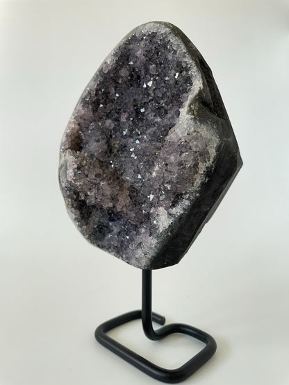 A 5-inch Brazilian amethyst cluster with purple hues and large crystals on a black metal stand with a white background.