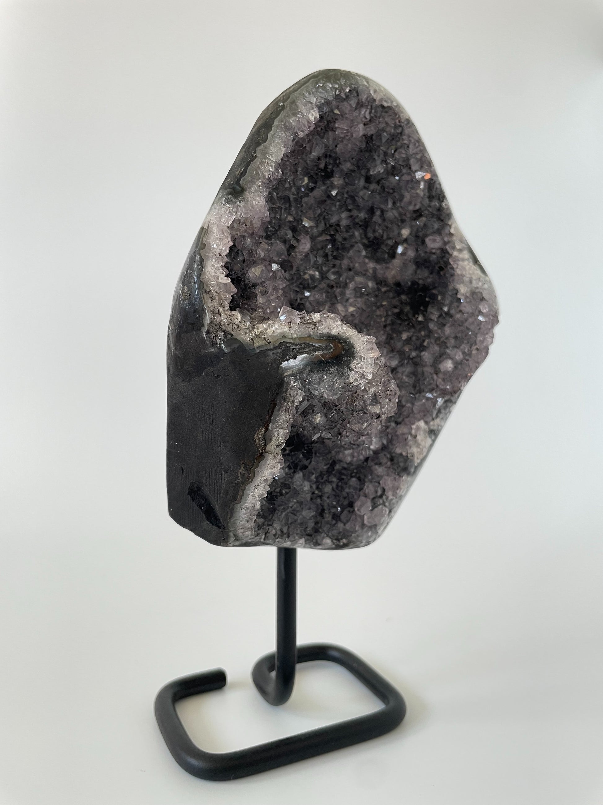 A 5-inch Brazilian amethyst cluster with purple hues and large crystals on a black metal stand with a white background.