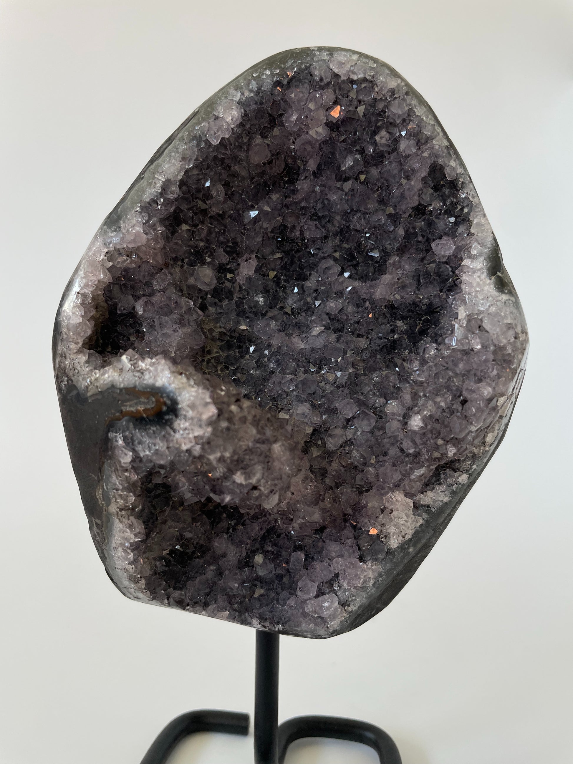 A 5-inch Brazilian amethyst cluster with purple hues and large crystals on a black metal stand with a white background.