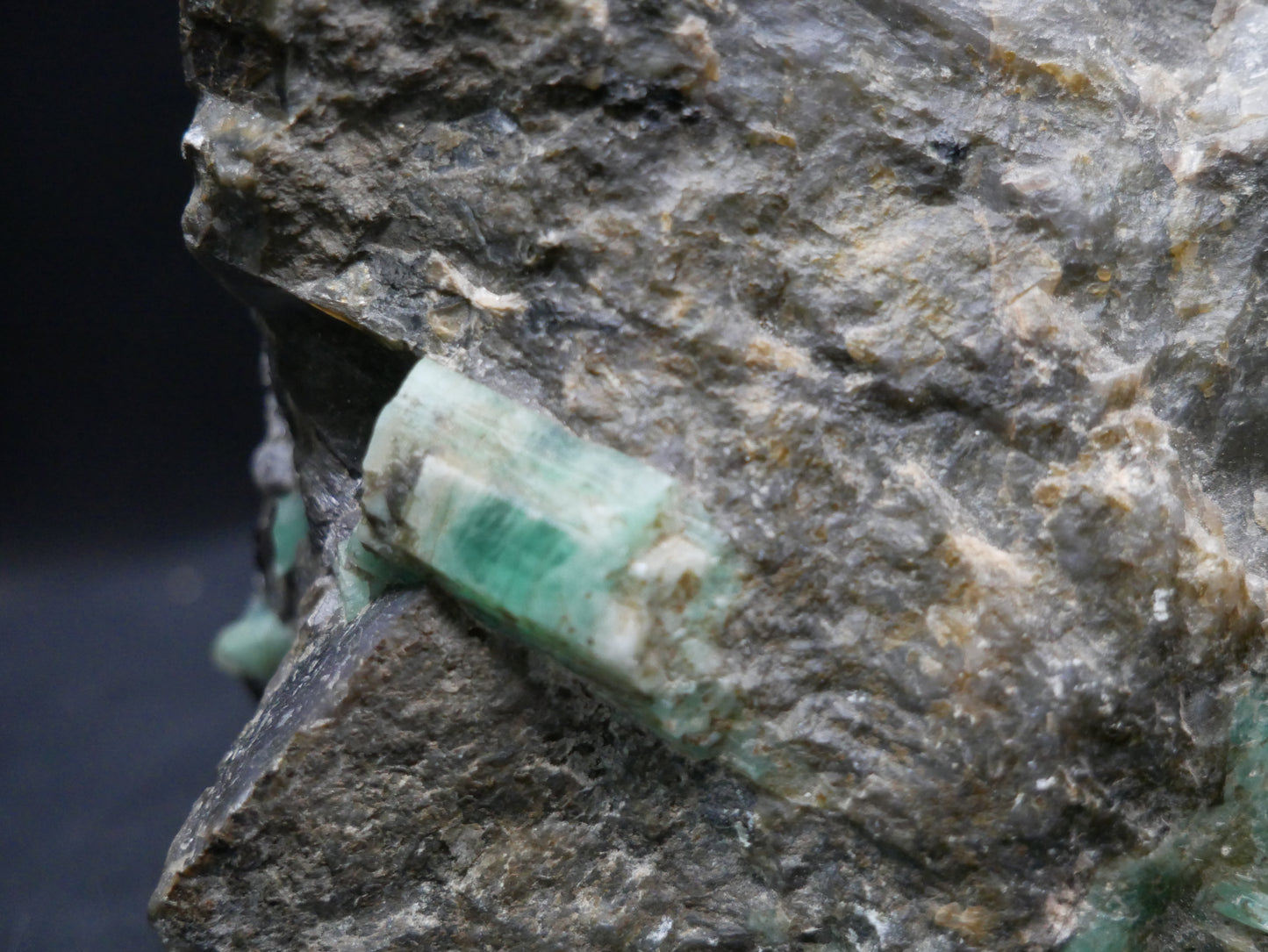 A large emerald in a matrix with distinctive emeralds protruding from the matrix on a black background.