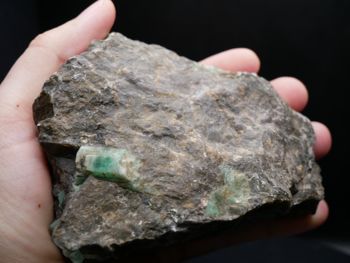 A large emerald in a matrix with distinctive emeralds protruding from the matrix on a black background.