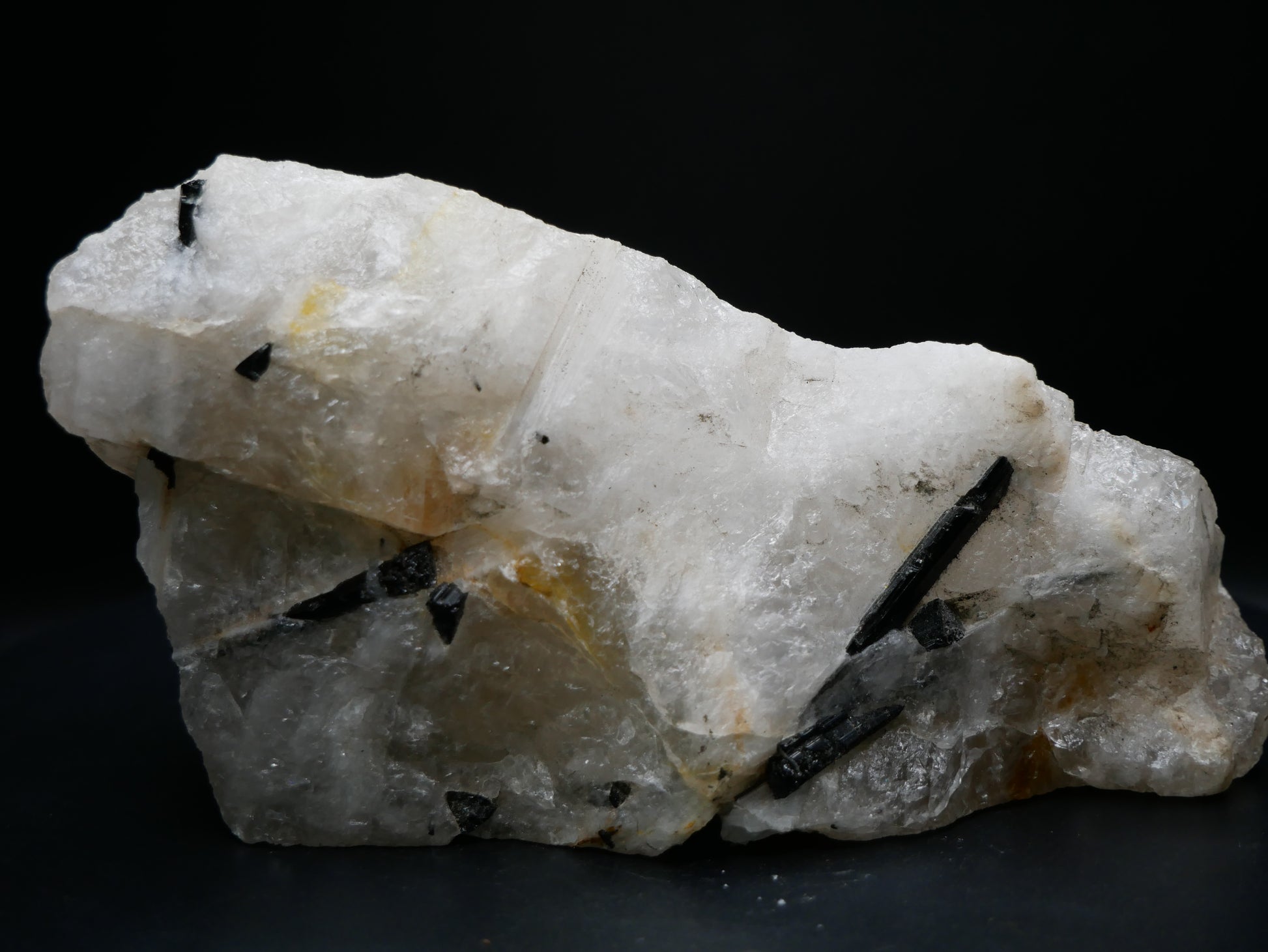 A black tourmaline in a matrix with a distinctive tourmaline crystal protruding from the matrix on a black background.