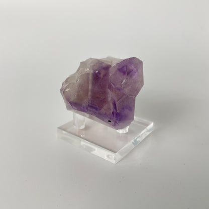 A close-up photo of a Brazilian amethyst point, weighing 6.7 ounces and measuring 2 inches in length. The crystal has a rich purple hue with natural variations in color and texture, showcasing its raw beauty.