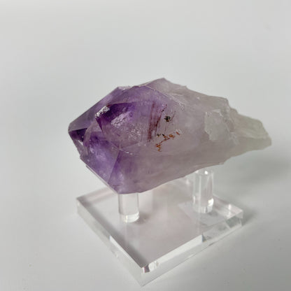 A close-up photo of a Brazilian amethyst point, weighing 6.7 ounces and measuring 2 inches in length. The crystal has a rich purple hue with natural variations in color and texture, showcasing its raw beauty.