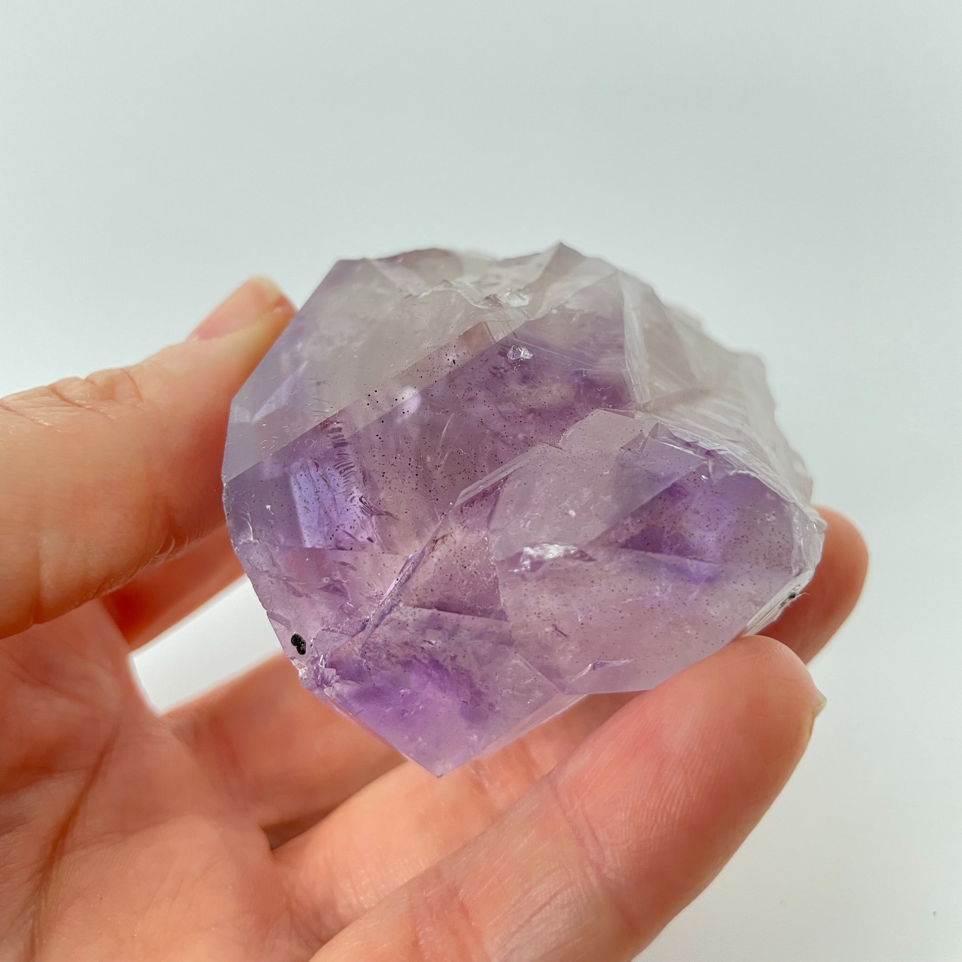 A close-up photo of a Brazilian amethyst point, weighing 6.7 ounces and measuring 2 inches in length. The crystal has a rich purple hue with natural variations in color and texture, showcasing its raw beauty.