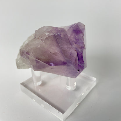 A close-up photo of a Brazilian amethyst point, weighing 6.7 ounces and measuring 2 inches in length. The crystal has a rich purple hue with natural variations in color and texture, showcasing its raw beauty.