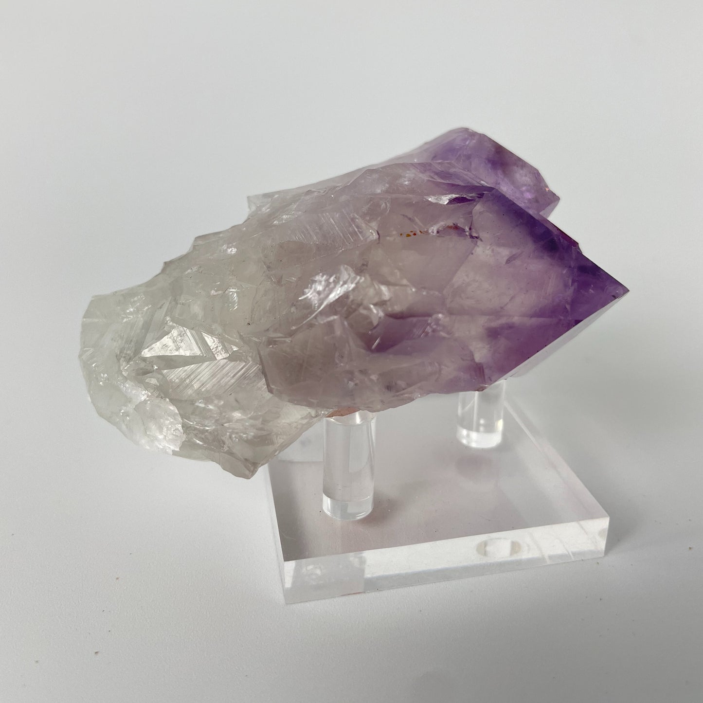 A close-up photo of a Brazilian amethyst point, weighing 6.7 ounces and measuring 2 inches in length. The crystal has a rich purple hue with natural variations in color and texture, showcasing its raw beauty.