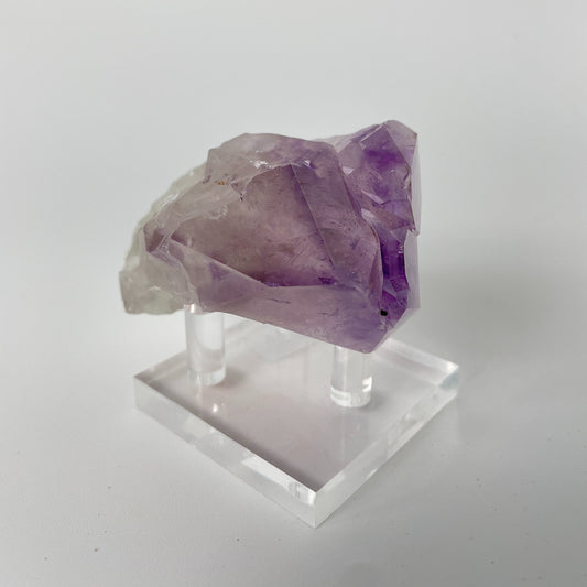 A close-up photo of a Brazilian amethyst point, weighing 6.7 ounces and measuring 2 inches in length. The crystal has a rich purple hue with natural variations in color and texture, showcasing its raw beauty.