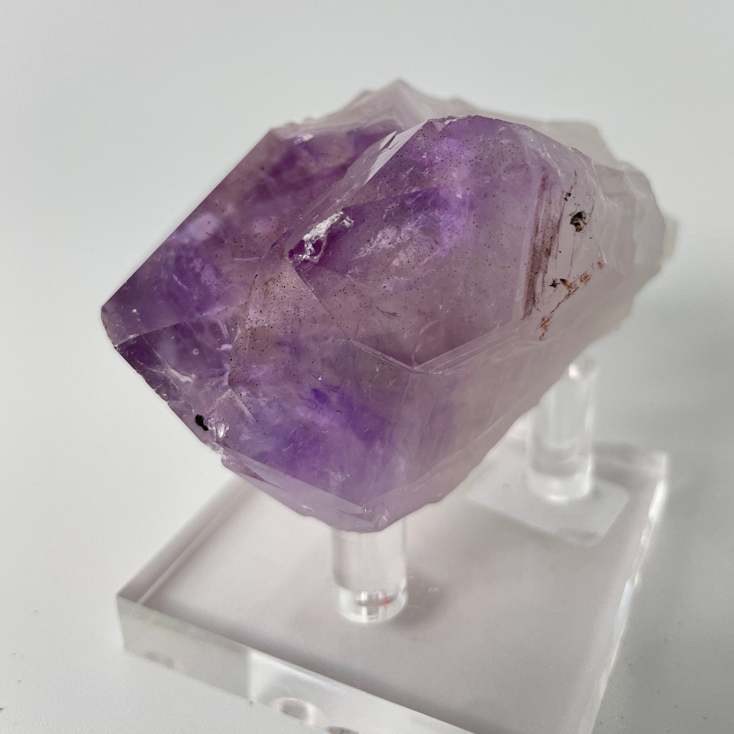 A close-up photo of a Brazilian amethyst point, weighing 6.7 ounces and measuring 2 inches in length. The crystal has a rich purple hue with natural variations in color and texture, showcasing its raw beauty.