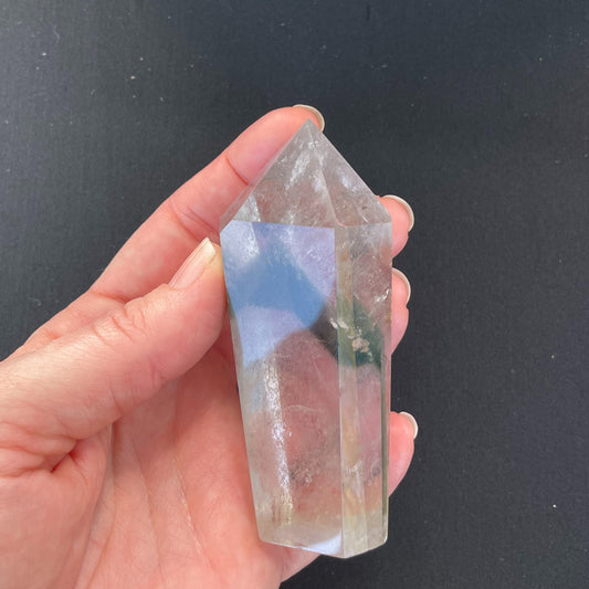 A close-up image of a garden quartz crystal point, measuring nearly two inches in length. The crystal exhibits intricate patterns of mineral inclusions resembling a garden landscape, with green chlorite and other minerals creating a picturesque scene within the transparent quartz.