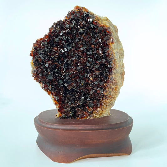 Large citrine cluster with deep orange-colored crystal formations on a brown wooden stand against a white background.