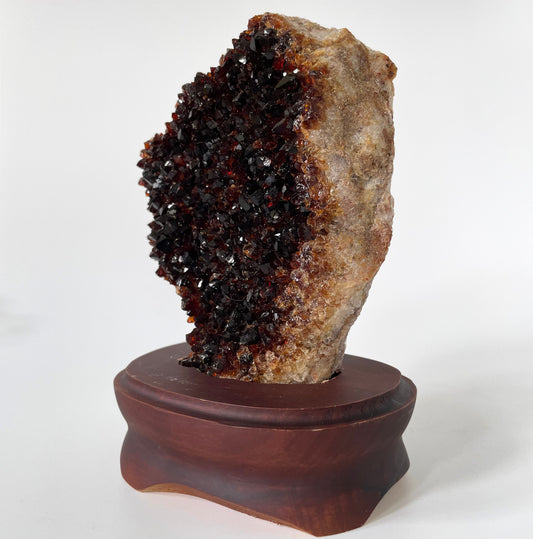 Large citrine cluster with deep orange-colored crystal formations on a brown wooden stand against a white background.