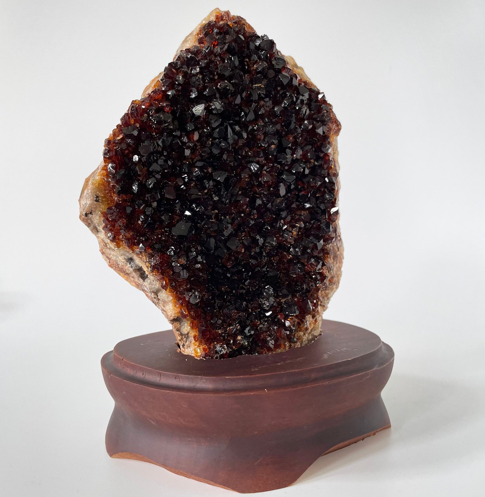 Large citrine cluster with deep orange-colored crystal formations on a brown wooden stand against a white background. 