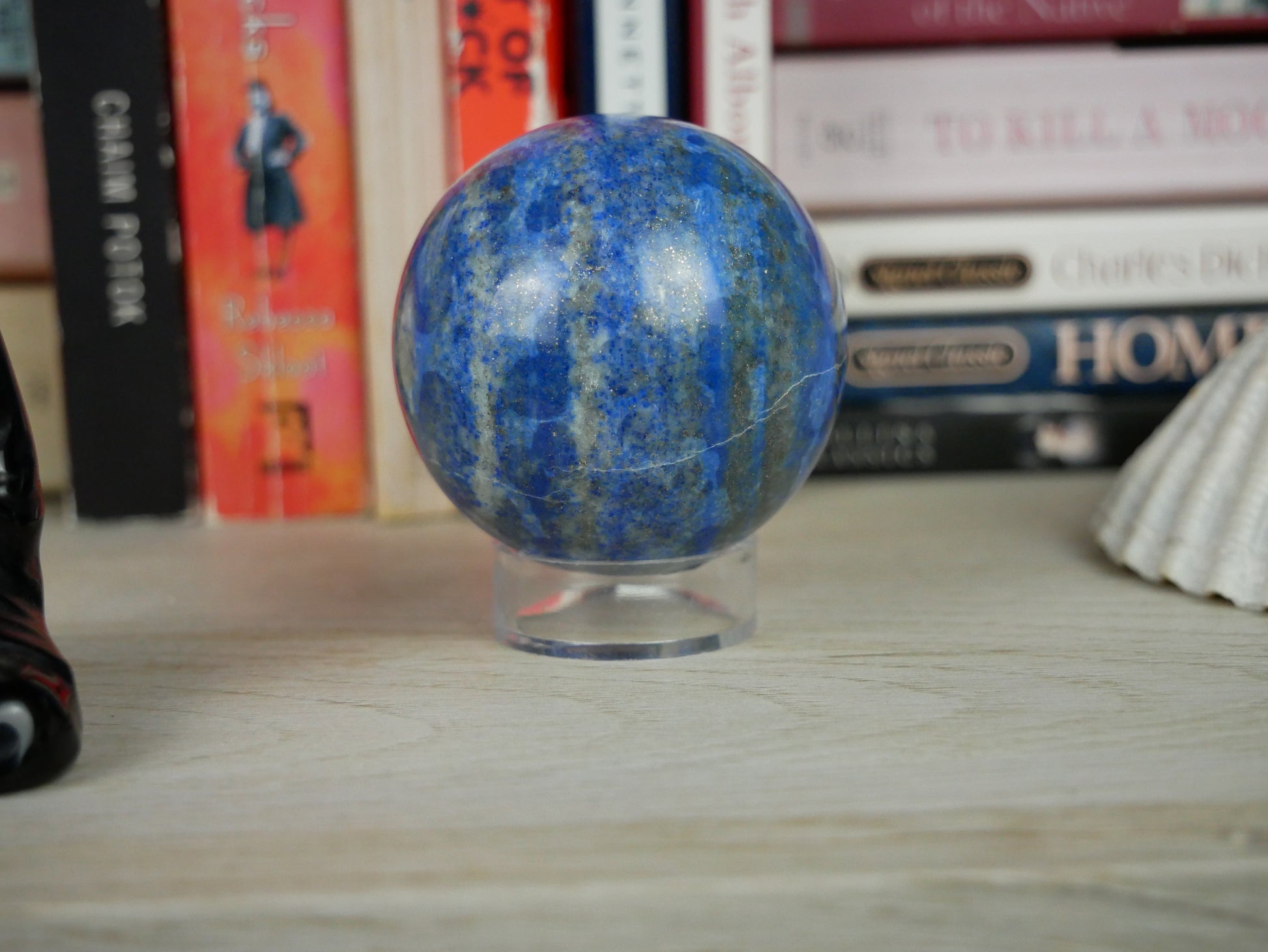 Close-up photo of a 2-inch diameter Lapis Lazuli sphere resting on a white surface. The deep blue hue of the sphere is interspersed with flecks of pyrite, creating a captivating celestial-like appearance. Light reflects off the polished surface, highlighting the stone's natural beauty.