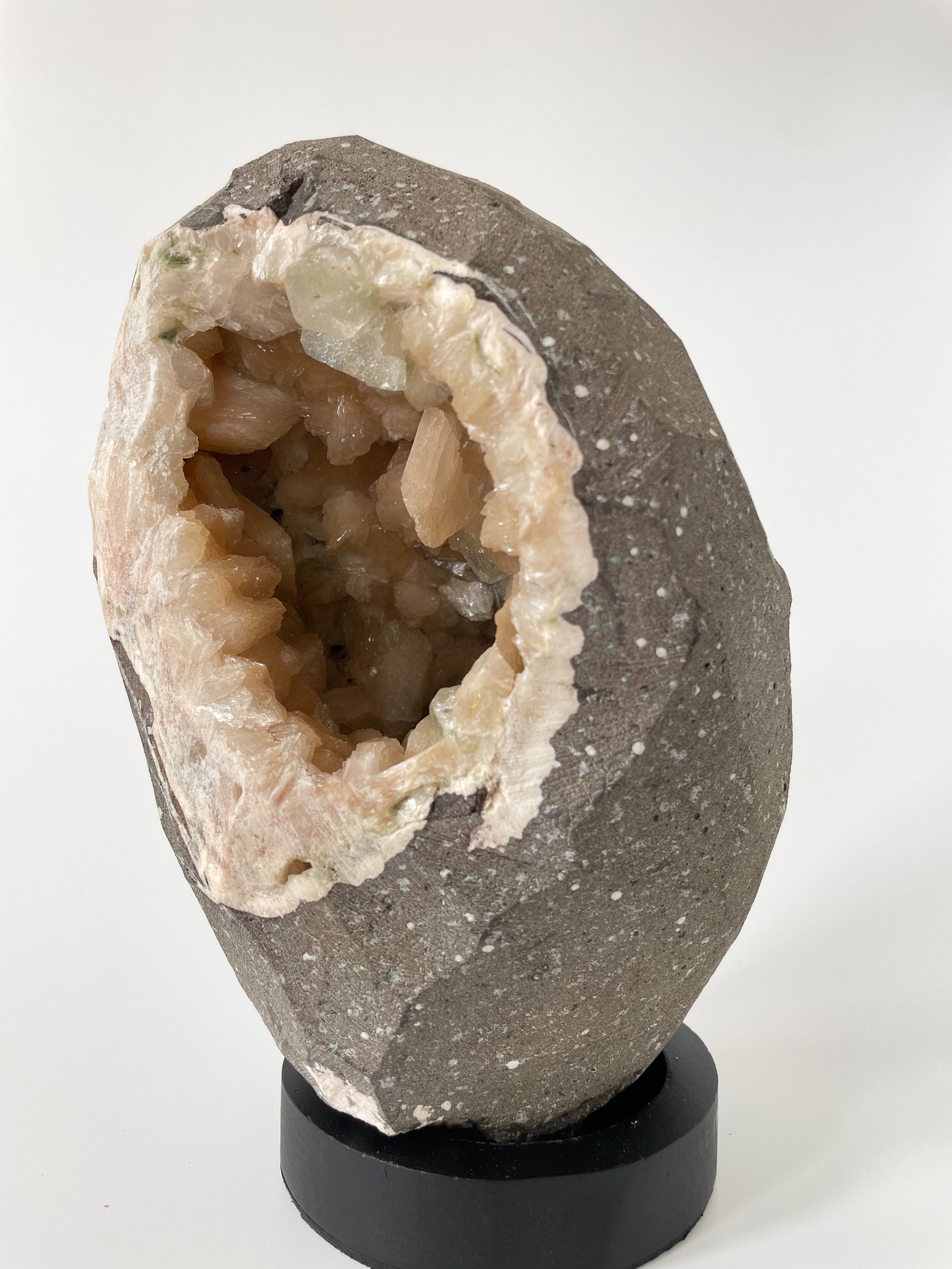 Close-up of the inside of a large stilbite geode with peach crystals and several green apophyllite crystals.