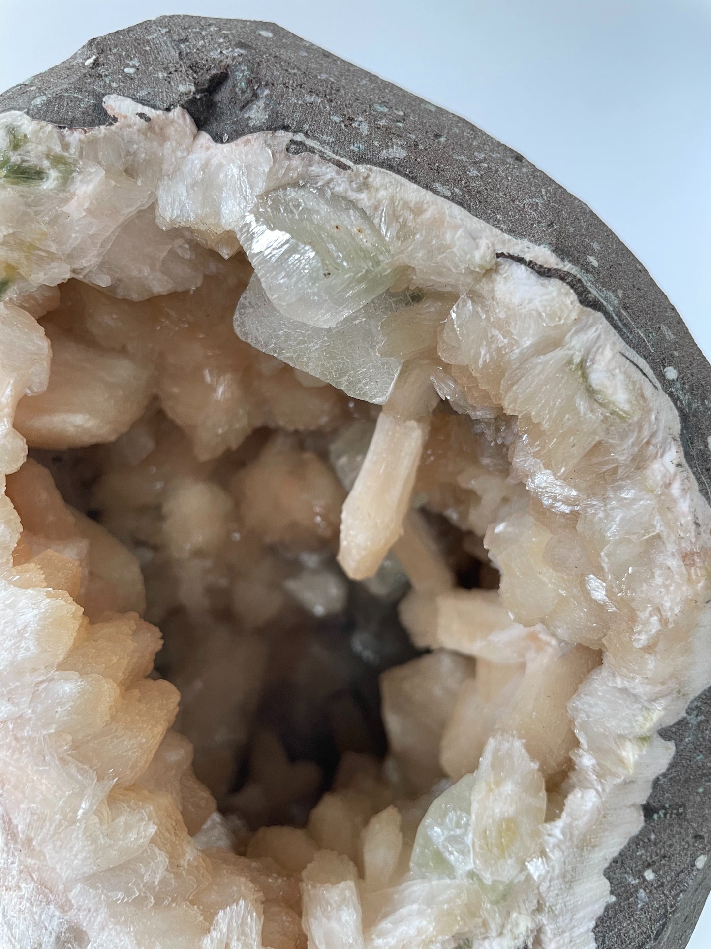 Close-up of the inside of a large stilbite geode with peach crystals and several green apophyllite crystals.