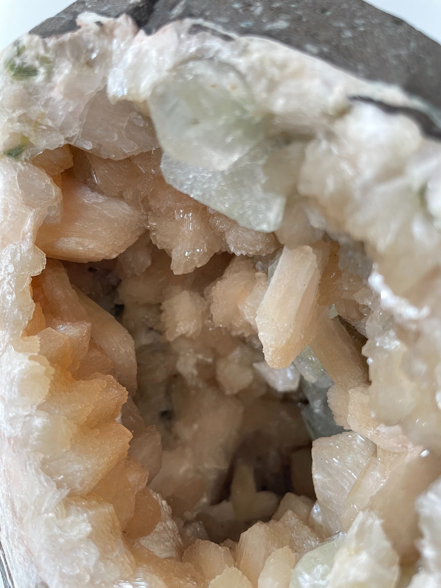 Close-up of the inside of a large stilbite geode with peach crystals and several green apophyllite crystals.