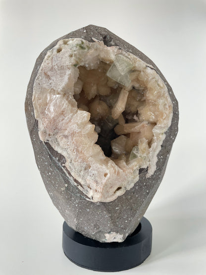 Close-up of the inside of a large stilbite geode with peach crystals and several green apophyllite crystals.