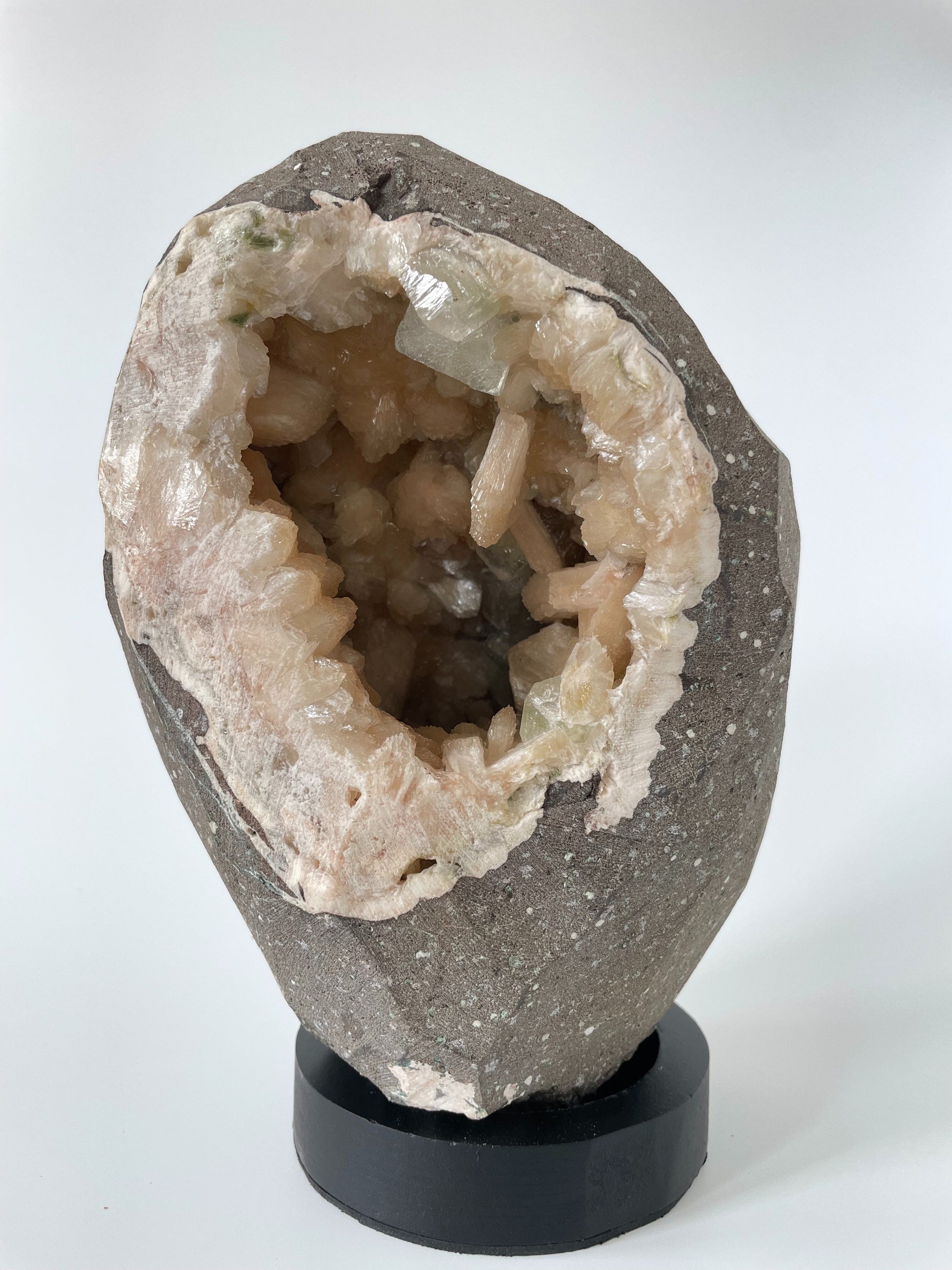 Close-up of the inside of a large stilbite geode with peach crystals and several green apophyllite crystals.