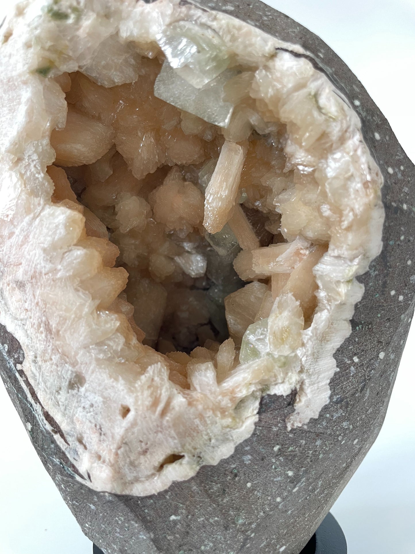 Close-up of the inside of a large stilbite geode with peach crystals and several green apophyllite crystals.