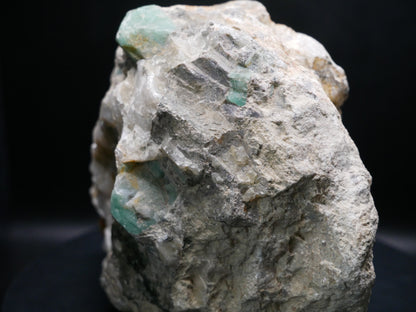 A large emerald in a matrix with distinctive emeralds protruding from the matrix on a black background.