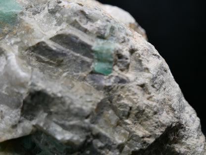 A large emerald in a matrix with distinctive emeralds protruding from the matrix on a black background.