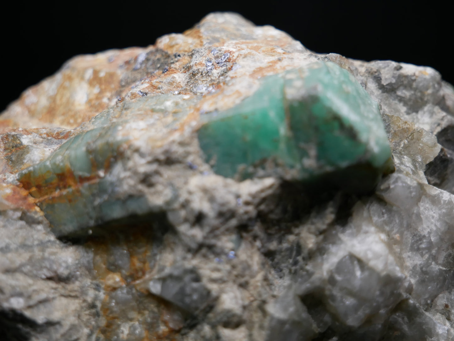 A large emerald in a matrix with distinctive emeralds protruding from the matrix on a black background.