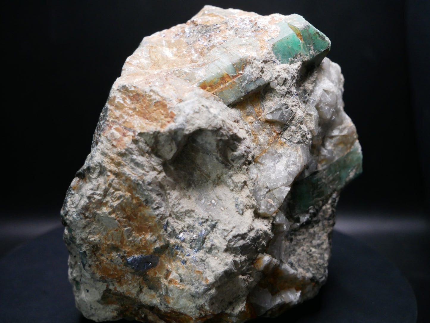 A large emerald in a matrix with distinctive emeralds protruding from the matrix on a black background.