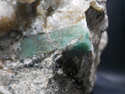 A large emerald in a matrix with distinctive emeralds protruding from the matrix on a black background.