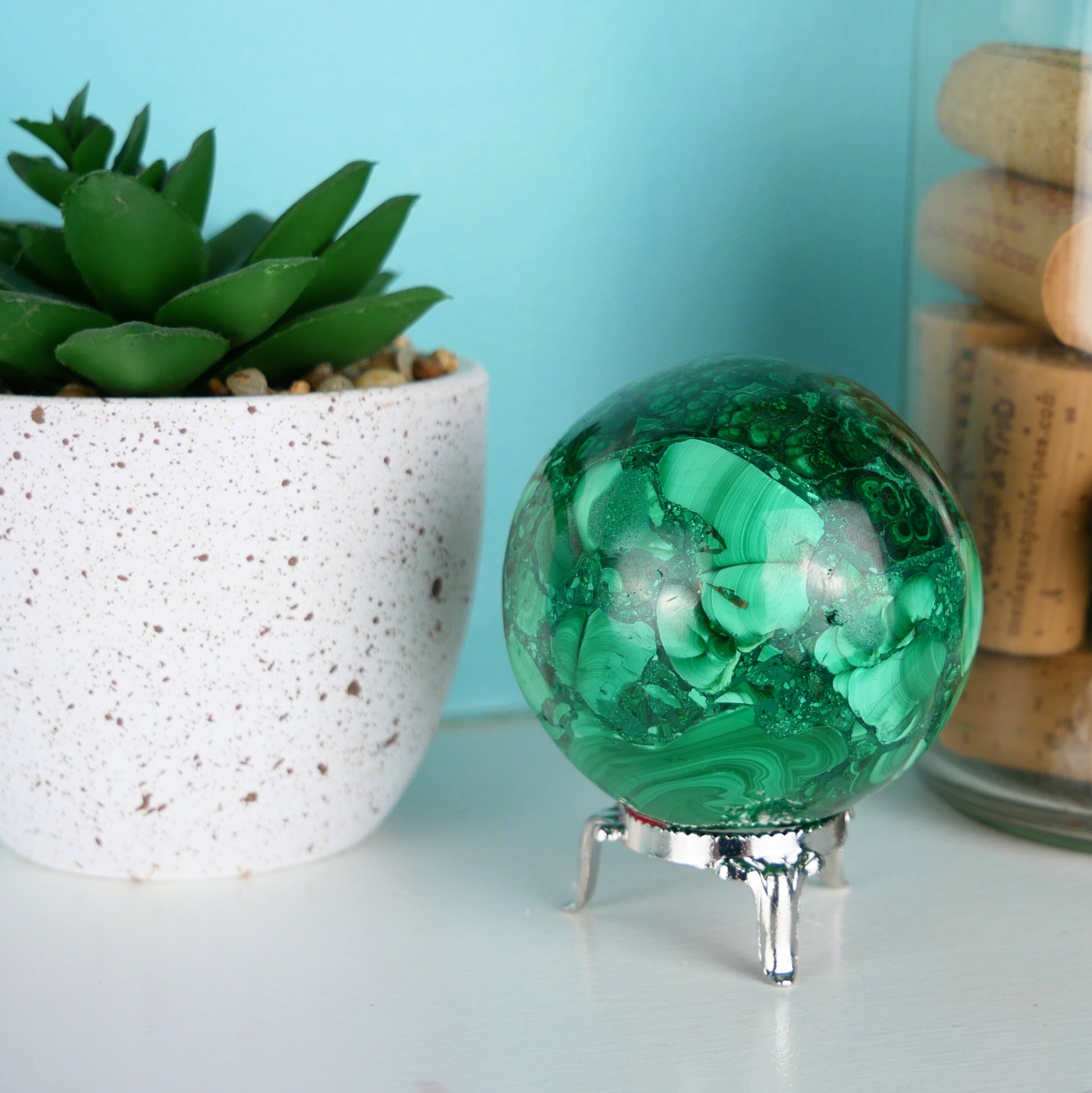 Close-up image of a 2.5-inch diameter Malachite Sphere, showcasing intricate green banding and natural patterns. The sphere rests on a reflective surface, highlighting its polished surface and vibrant coloration.