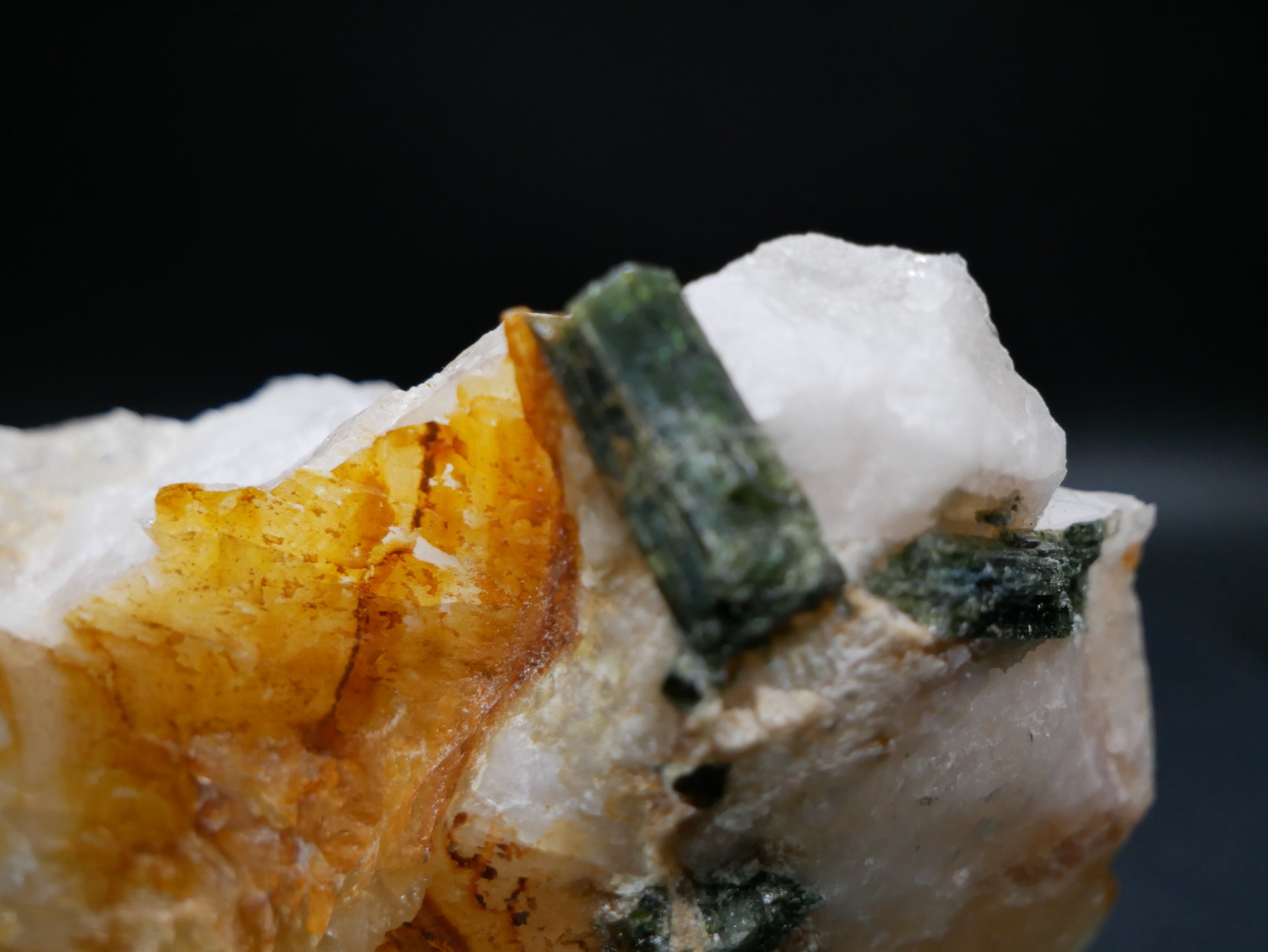 A large dark green tourmaline in a matrix with distinctive tourmaline crystals protruding from the matrix on a black background.