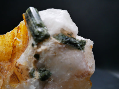 A large dark green tourmaline in a matrix with distinctive tourmaline crystals protruding from the matrix on a black background.