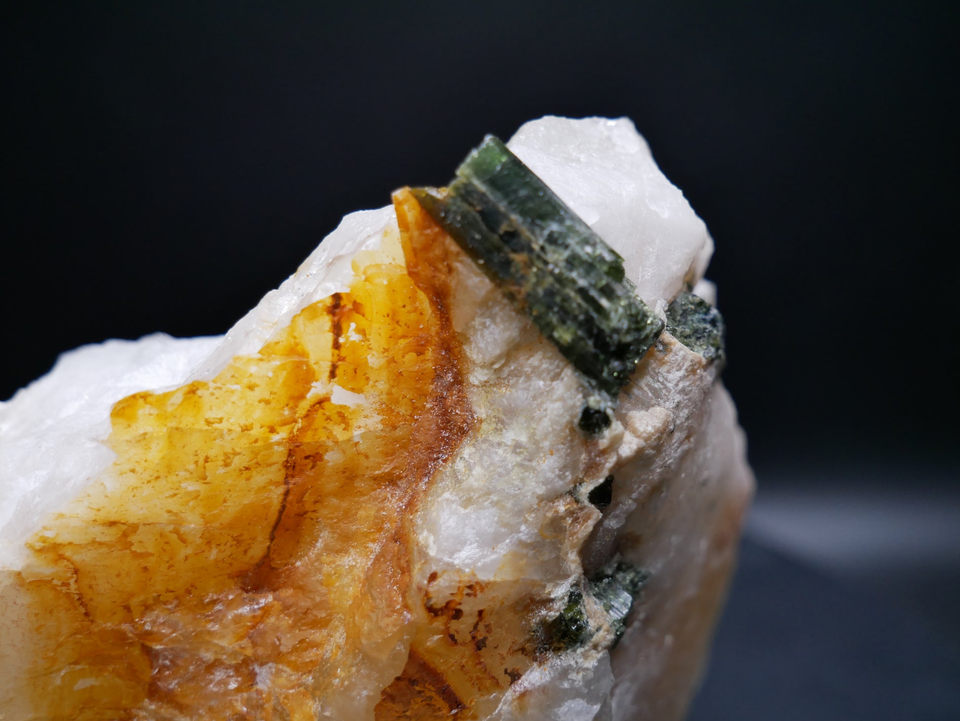 A large dark green tourmaline in a matrix with distinctive tourmaline crystals protruding from the matrix on a black background.