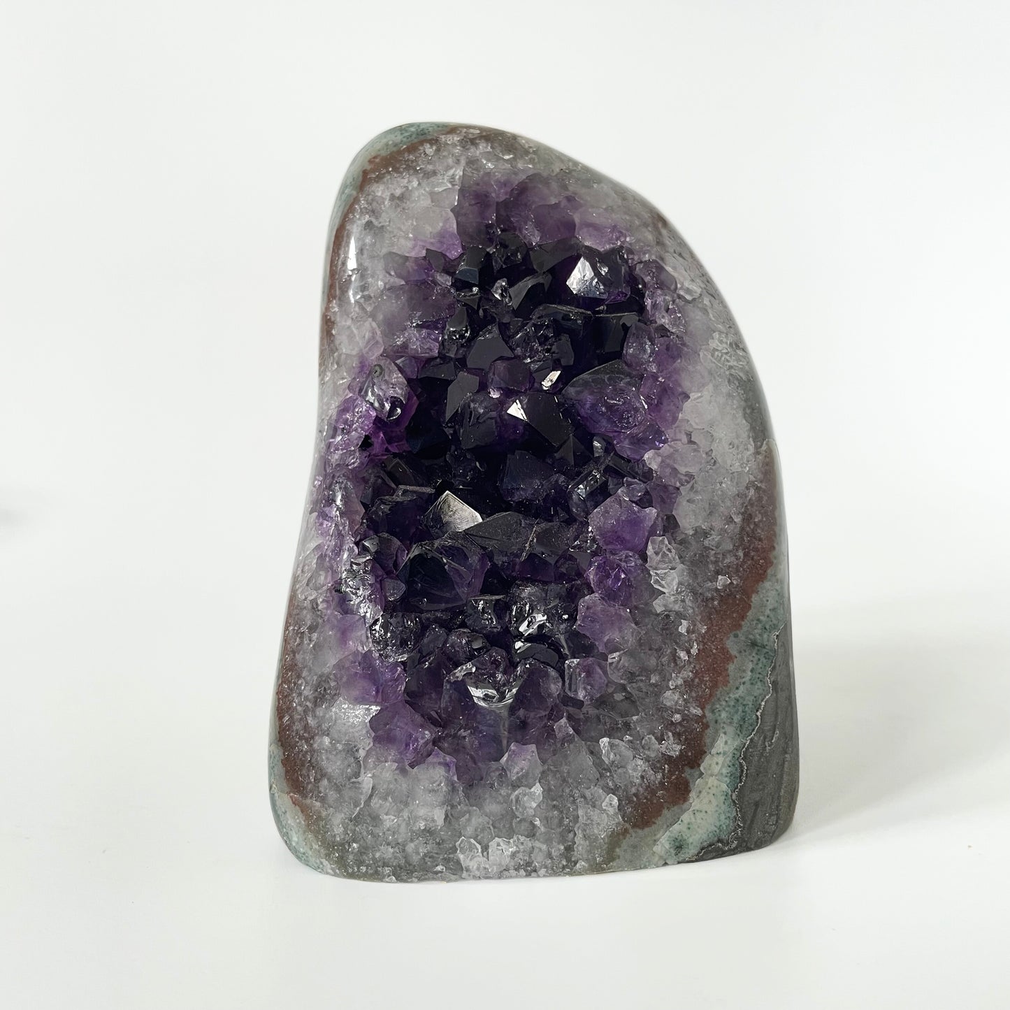 Amethyst cluster with polished edges and brilliant hues of deep purple and various sizes of crystal formations on a white background.