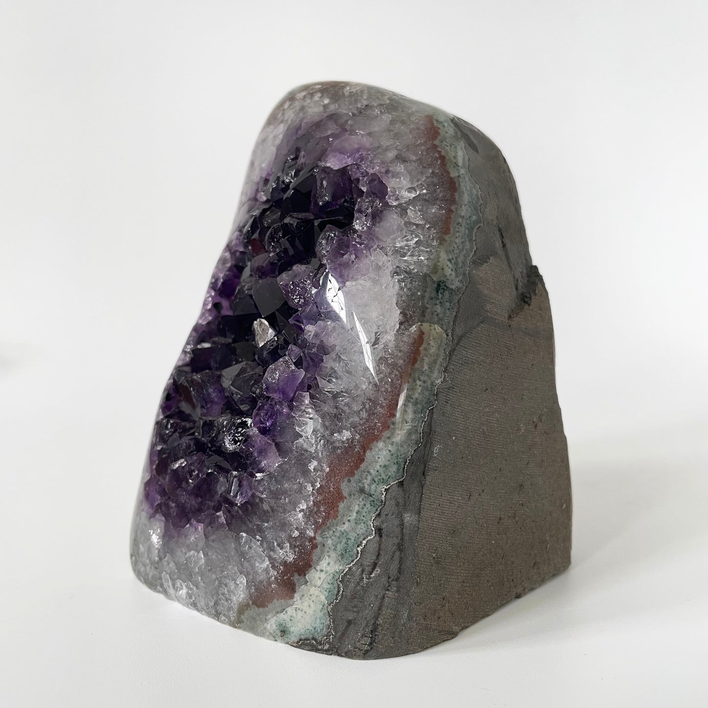 Amethyst cluster with polished edges and brilliant hues of deep purple and various sizes of crystal formations on a white background.