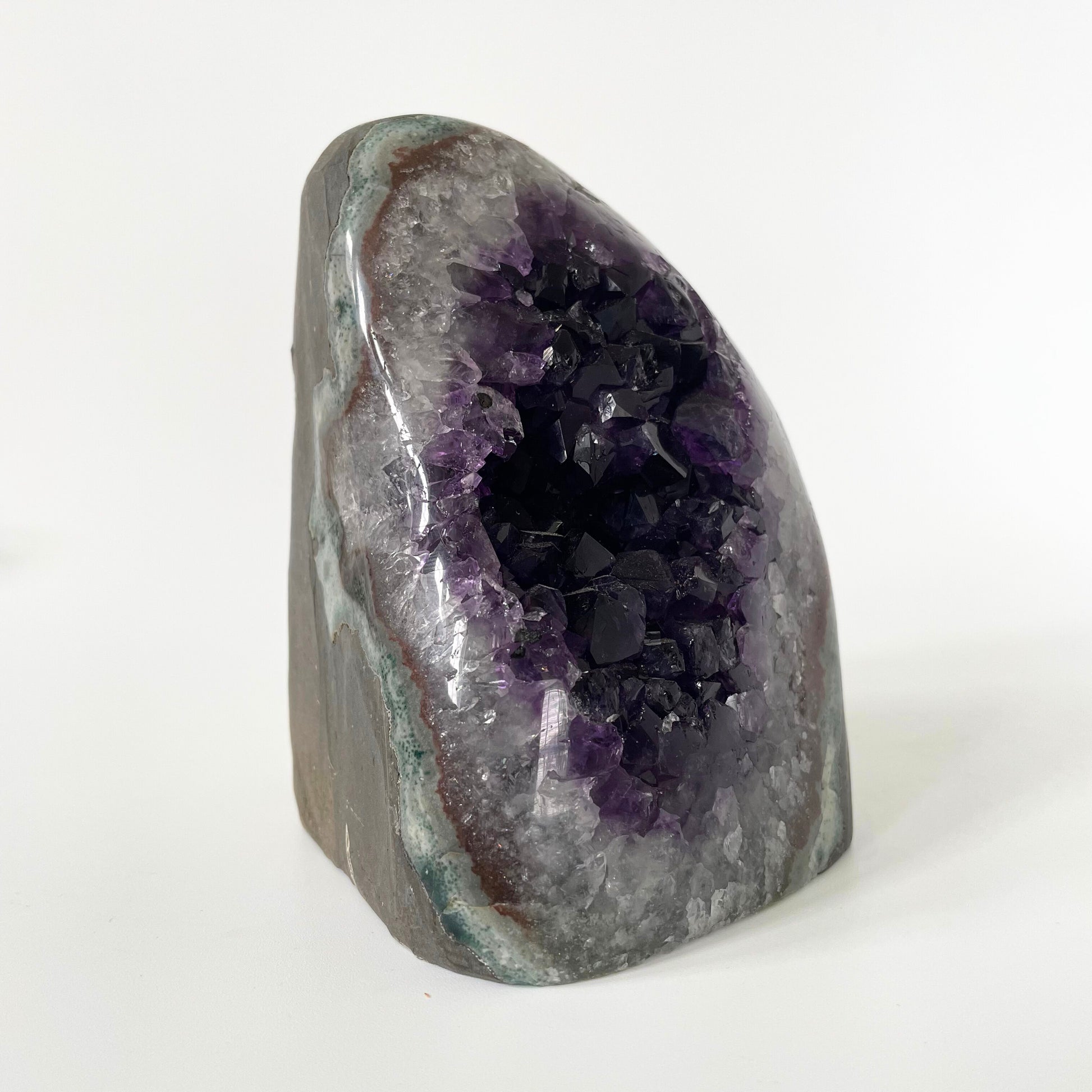 Amethyst cluster with polished edges and brilliant hues of deep purple and various sizes of crystal formations on a white background.